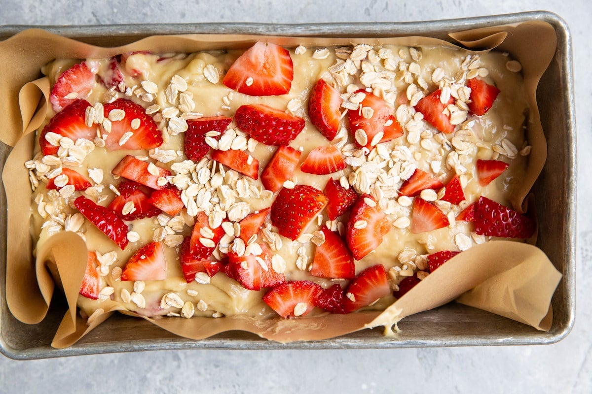 Loaf pan of muffin batter with chopped strawberries and oatmeal on top.