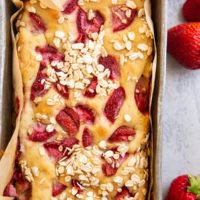 Bread pan with freshly baked strawberry banana bread inside and fresh strawberries to the side of the loaf.