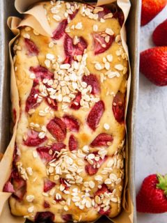 Bread pan with freshly baked strawberry banana bread inside and fresh strawberries to the side of the loaf.