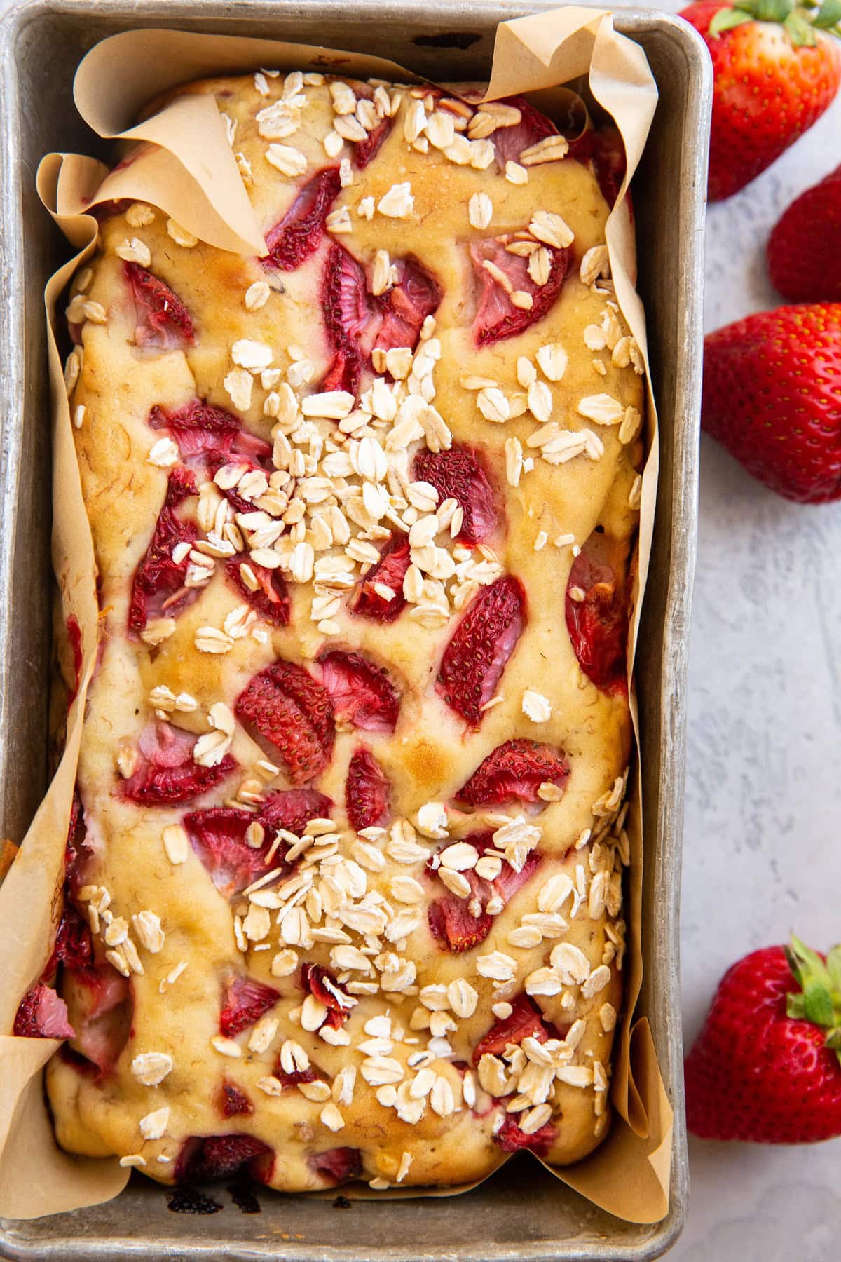 Bread pan with freshly baked strawberry banana bread inside and fresh strawberries to the side of the loaf.