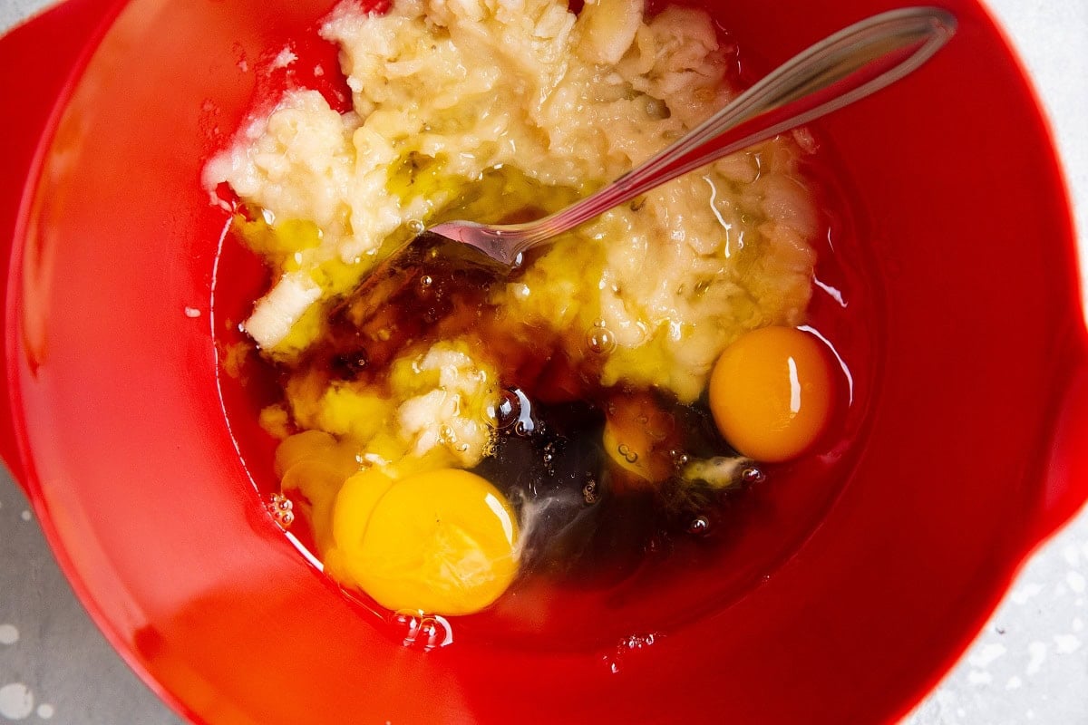 Wet ingredients for banana strawberry bread in a red mixing bowl.