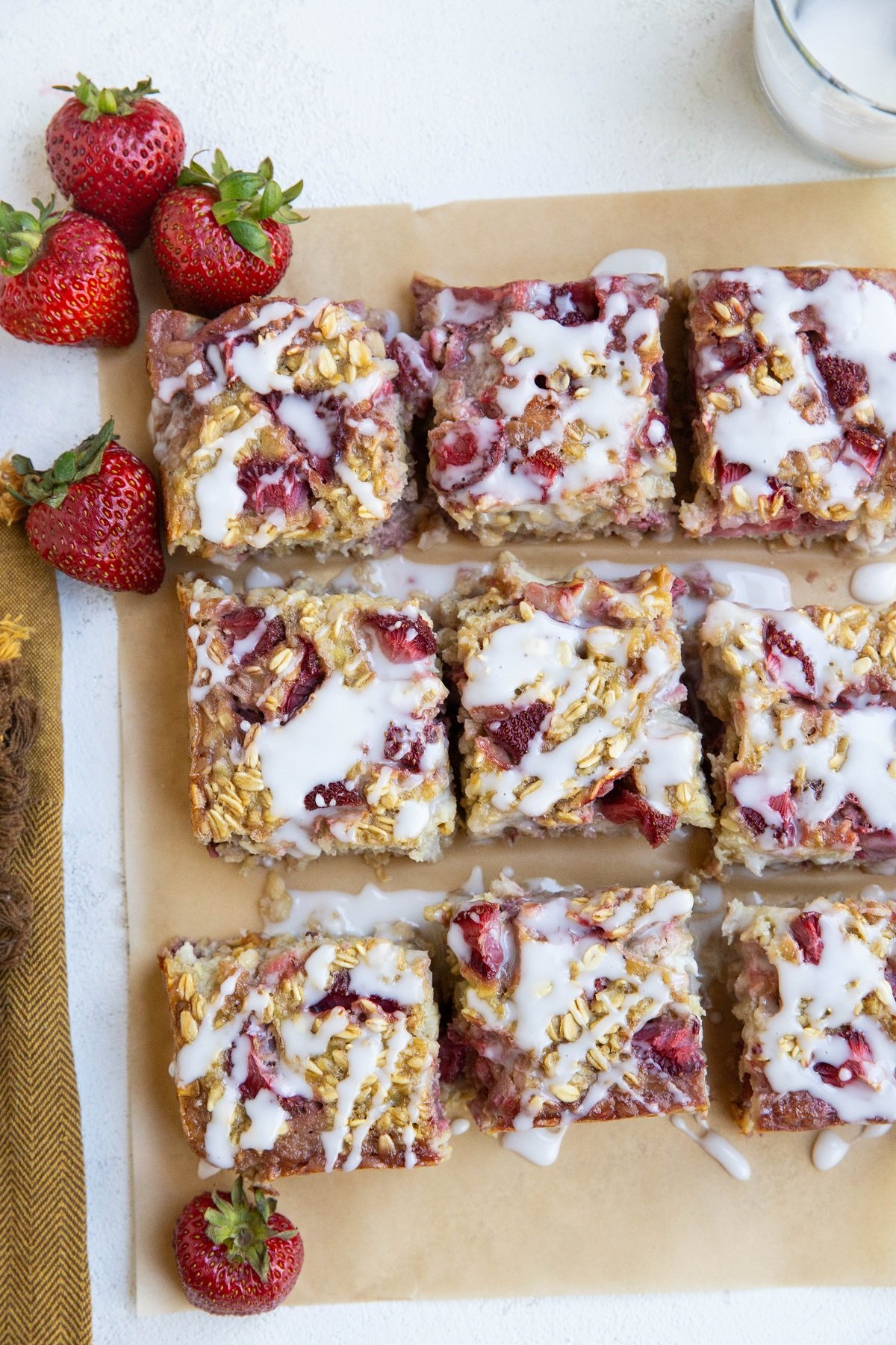 Slices of baked oatmeal on a sheet of parchment paper. Fresh strawberries and a napkin to the side.