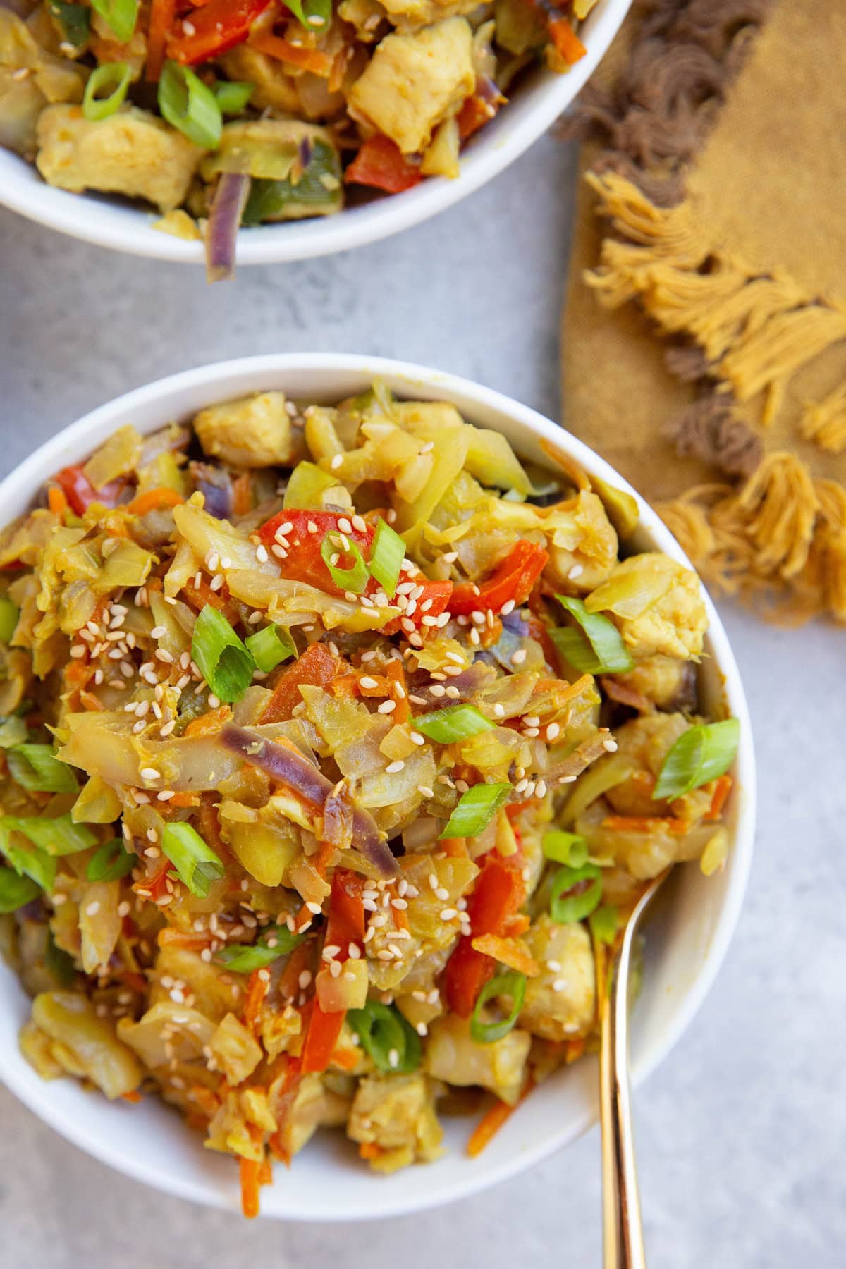 Two big bowls of Thai chicken and cabbage with a golden napkin to the side and a gold fork.