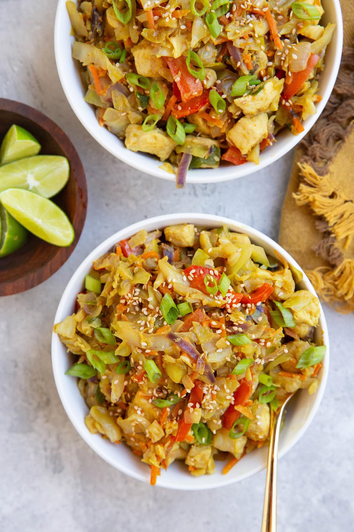 White bowls of Thai Chicken and Cabbage with a bowl of lime wedges to the side.