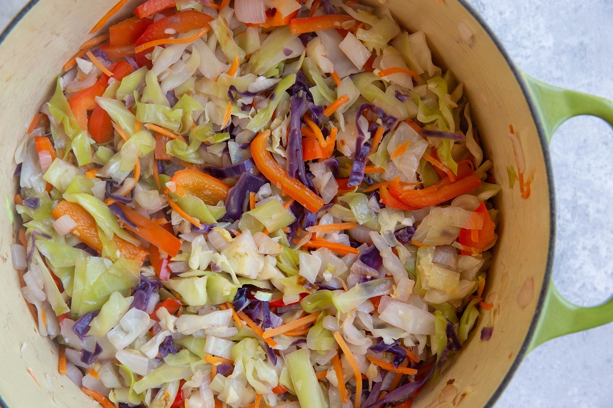 Cabbage, onion, carrots, and bell pepper cooking in a large pot.