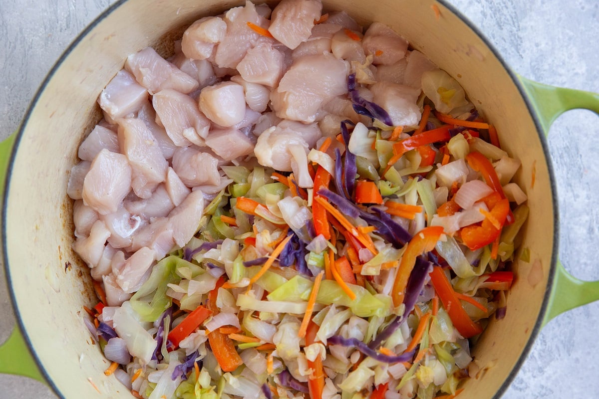 Vegetables in a pot off to the side with raw chopped chicken on the other half of the pot.