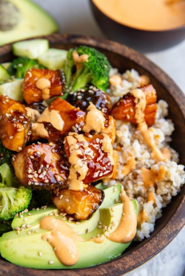 Bang bang salmon in a bowl with avocado, sauteed broccoli, and rice.