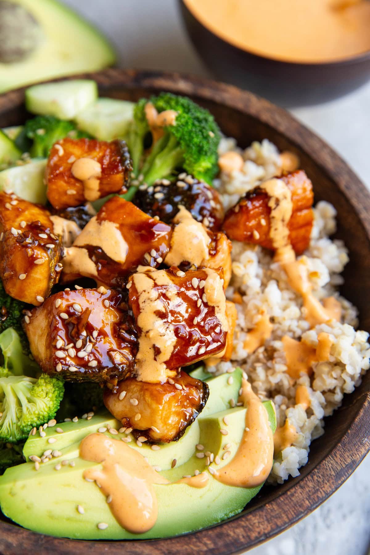 Bang bang salmon in a bowl with avocado, sauteed broccoli, and rice.