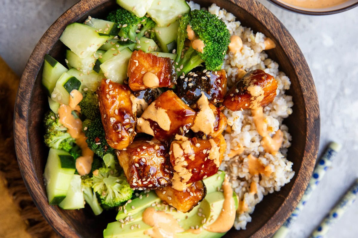 Wood bowl of brown rice, salmon bites, broccoli, and avocado and cucumbers.