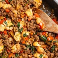 Ground beef and vegetables in a skillet with a wooden spoon, ready to serve.