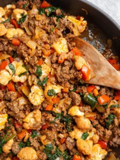 Ground beef and vegetables in a skillet with a wooden spoon, ready to serve.
