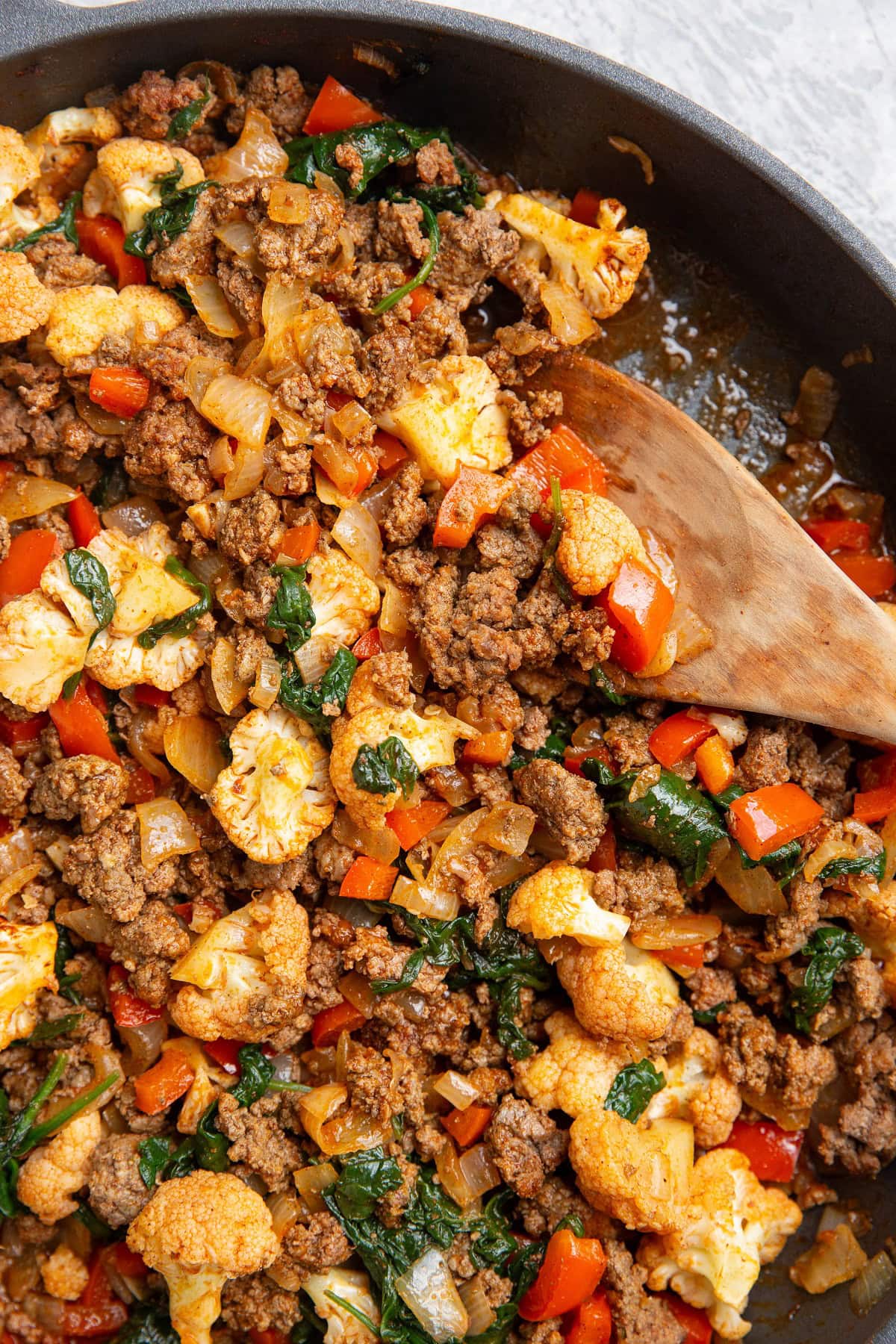 Ground beef and vegetables in a skillet with a wooden spoon, ready to serve.