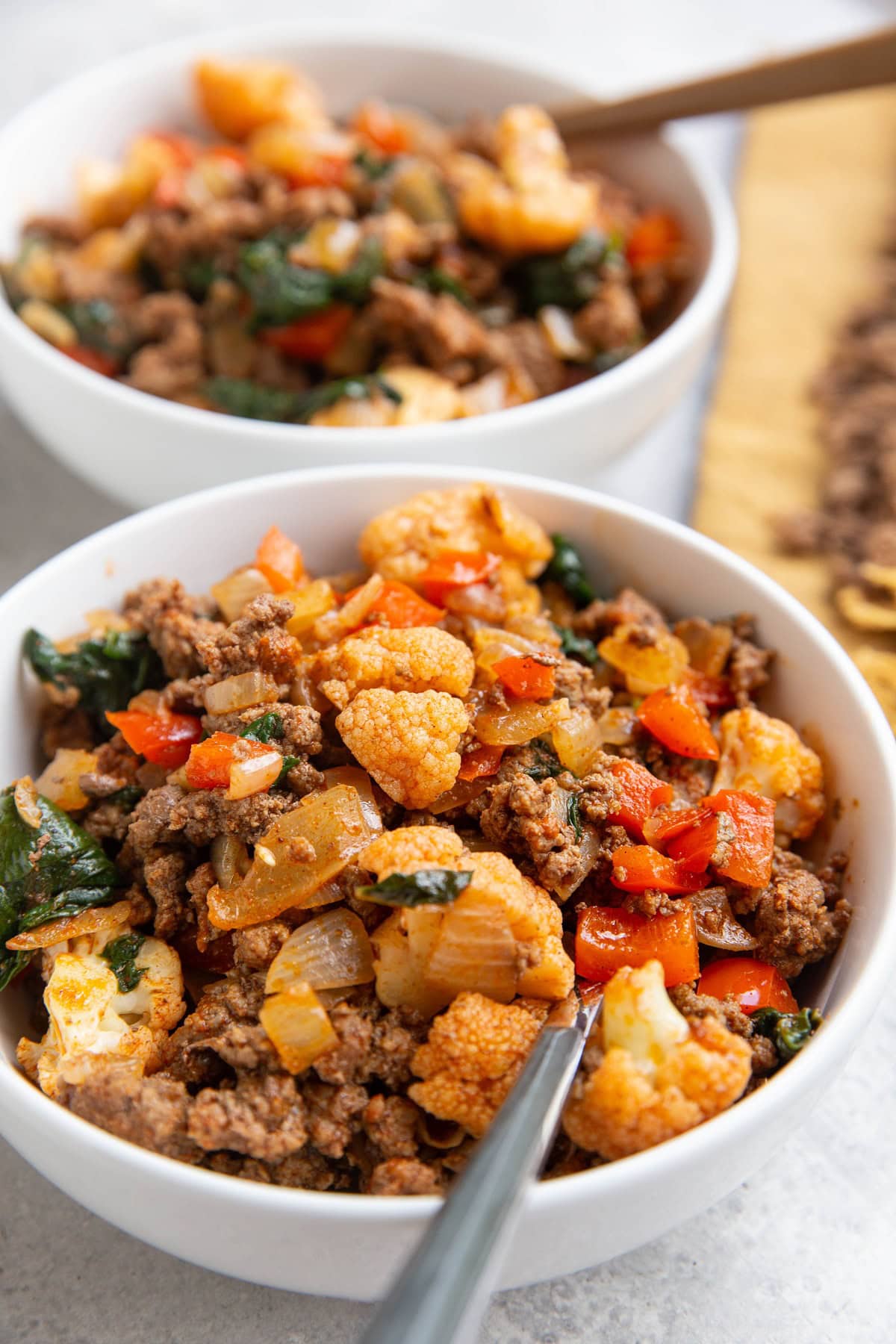 Two white bowls of ground beef and vegetables.