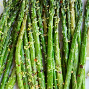 White plate of asparagus with lemon zest and pepper on top and fresh lemons to the side.