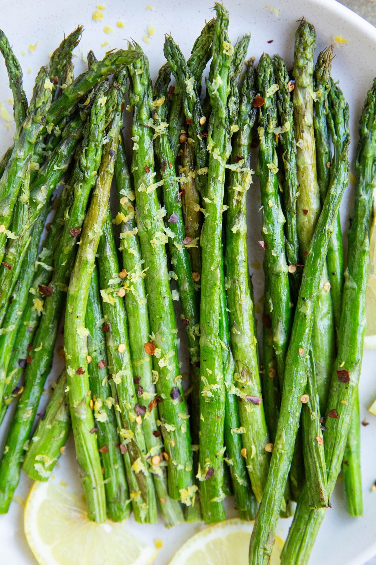 White plate of asparagus with lemon zest and pepper on top and fresh lemons to the side.