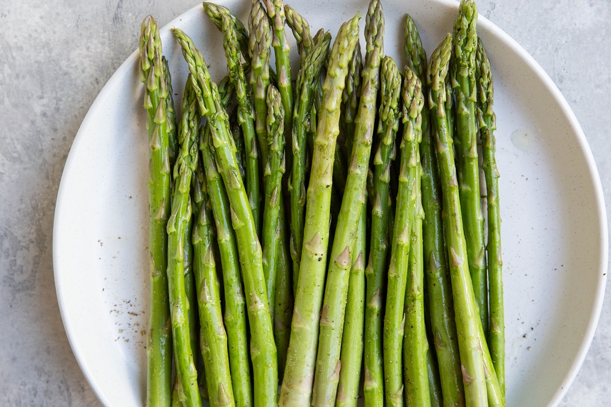 Raw asparagus on a plate drizzled in avocado oil with salt and pepper on top.