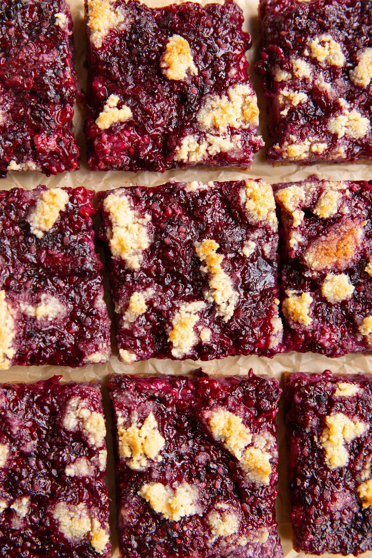 Blackberry Crumb Bars cut into individual portions on a sheet of parchment paper.
