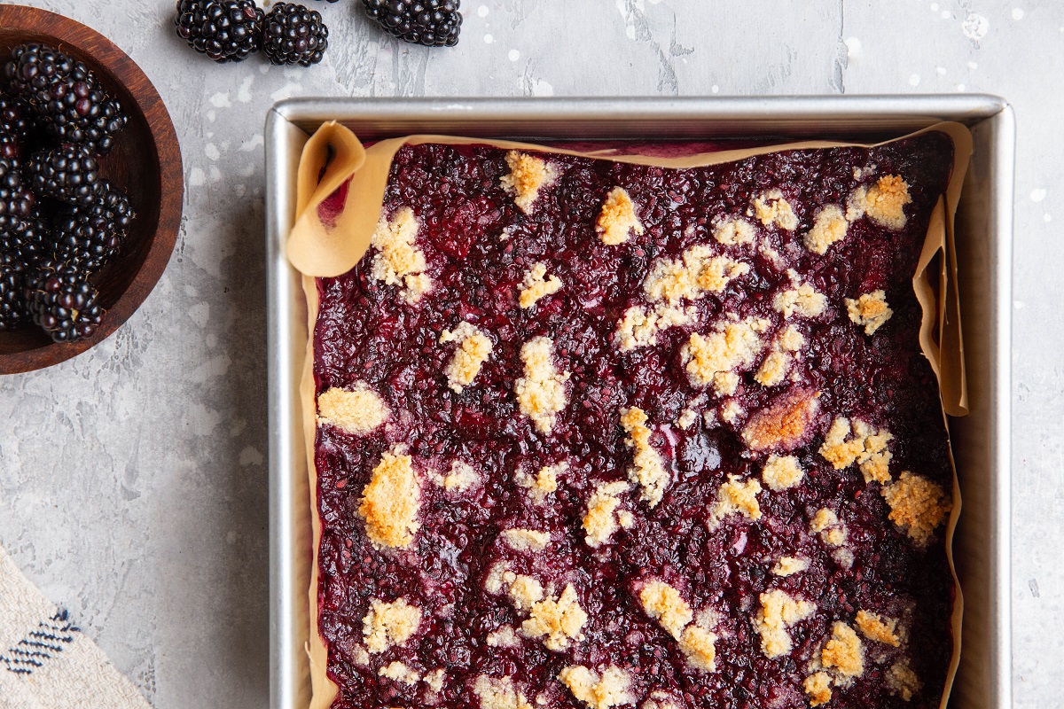 Grain-free blackberry bars in a baking pan, fresh out of the oven with a bowl of fresh blueberries to the side.