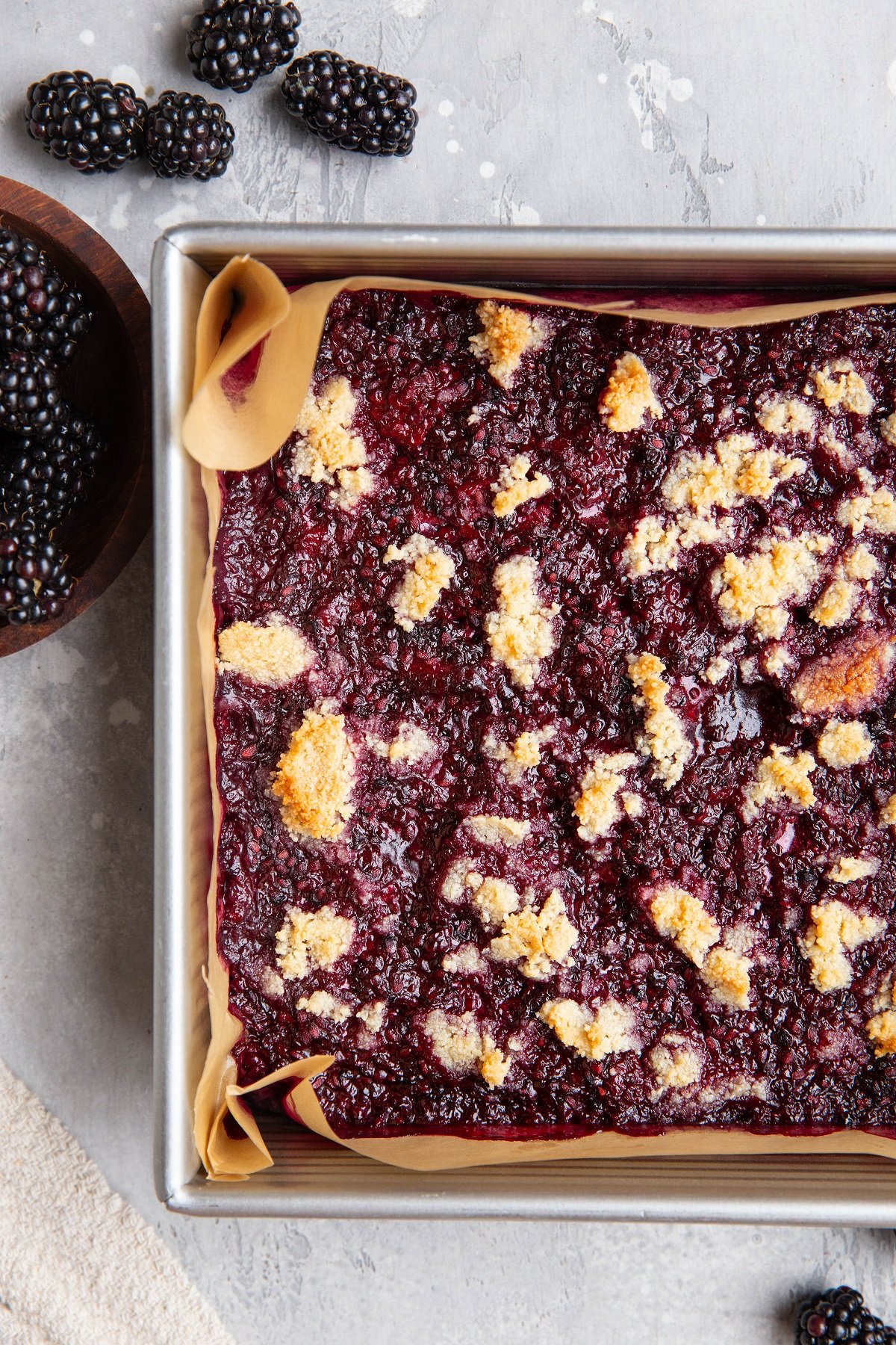 Baking pan of blackberry crumb bars with fresh blackberries to the side.