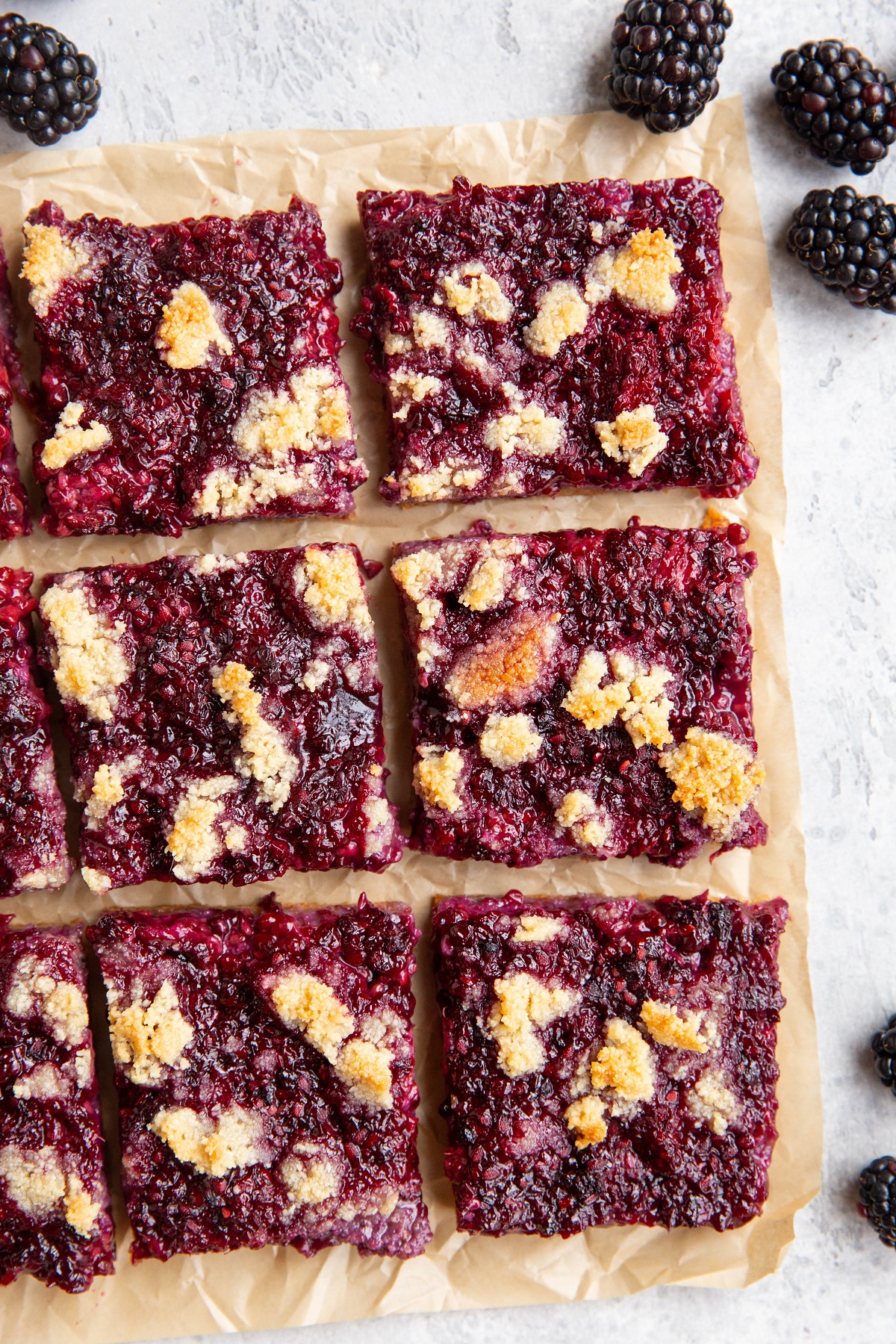 Sheet of parchment paper with blackberry bars on top with fresh blackberries all around.