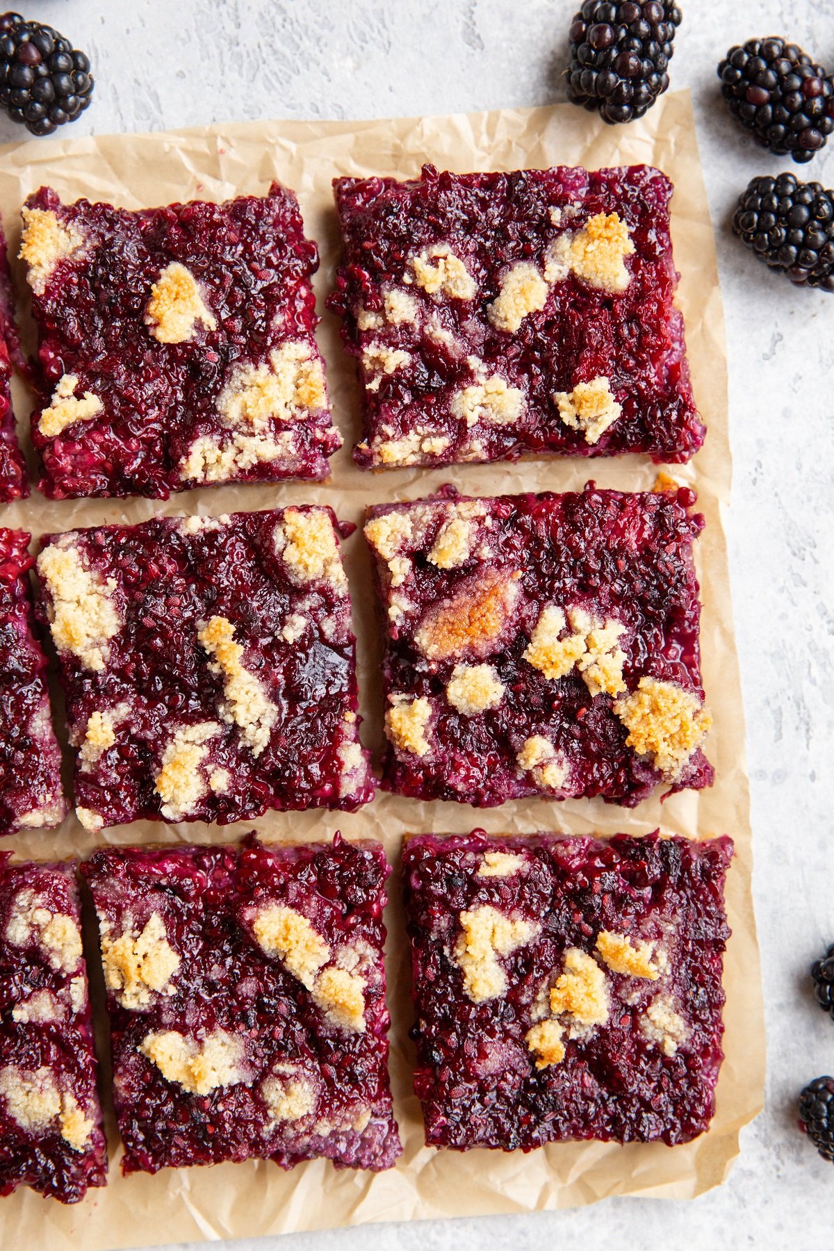 Sheet of parchment paper with blackberry bars on top with fresh blackberries all around.