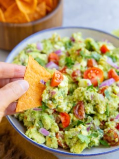 Hand holding a chip with avocado dip on top.