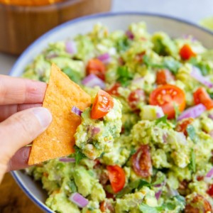 Hand holding a chip with avocado dip on top.