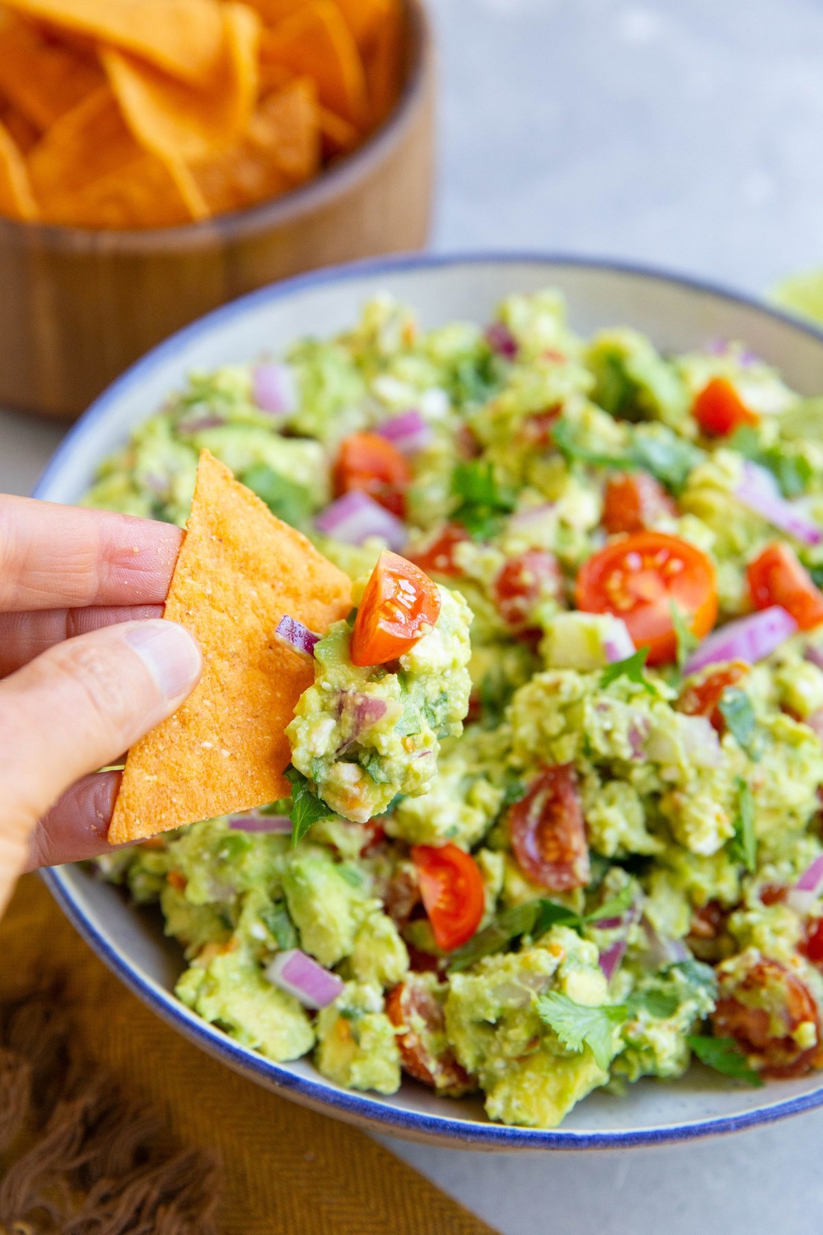 Hand holding a chip with avocado dip on top.