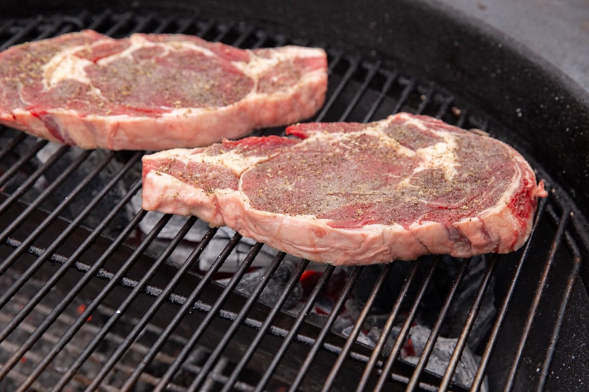 Two raw steaks on a grill, ready to be grilled.