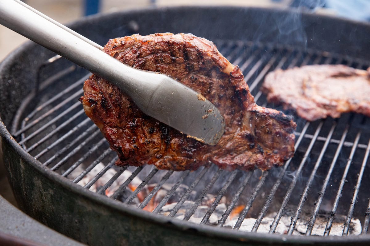 Tongs holding a steak sideways on the grill to sear the fat.