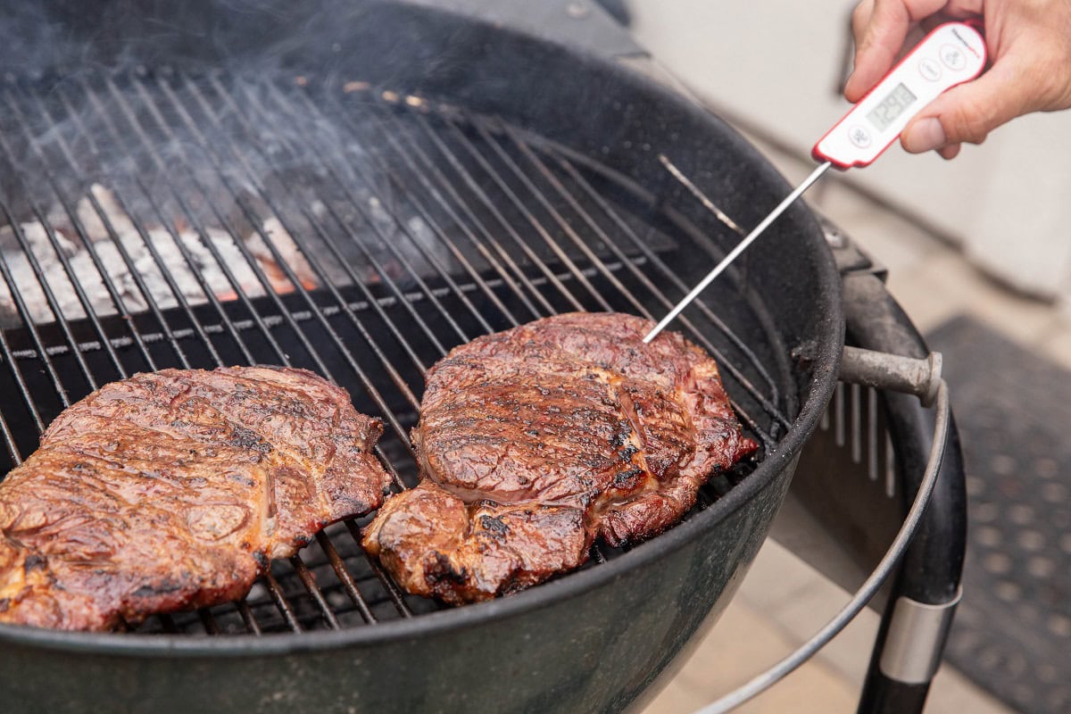 Hand inserting a thermometer into a steak to get a temperature read.