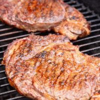 Two boneless ribeye steaks on a grill, finished and ready to eat.