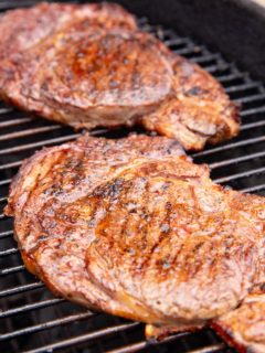 Two boneless ribeye steaks on a grill, finished and ready to eat.