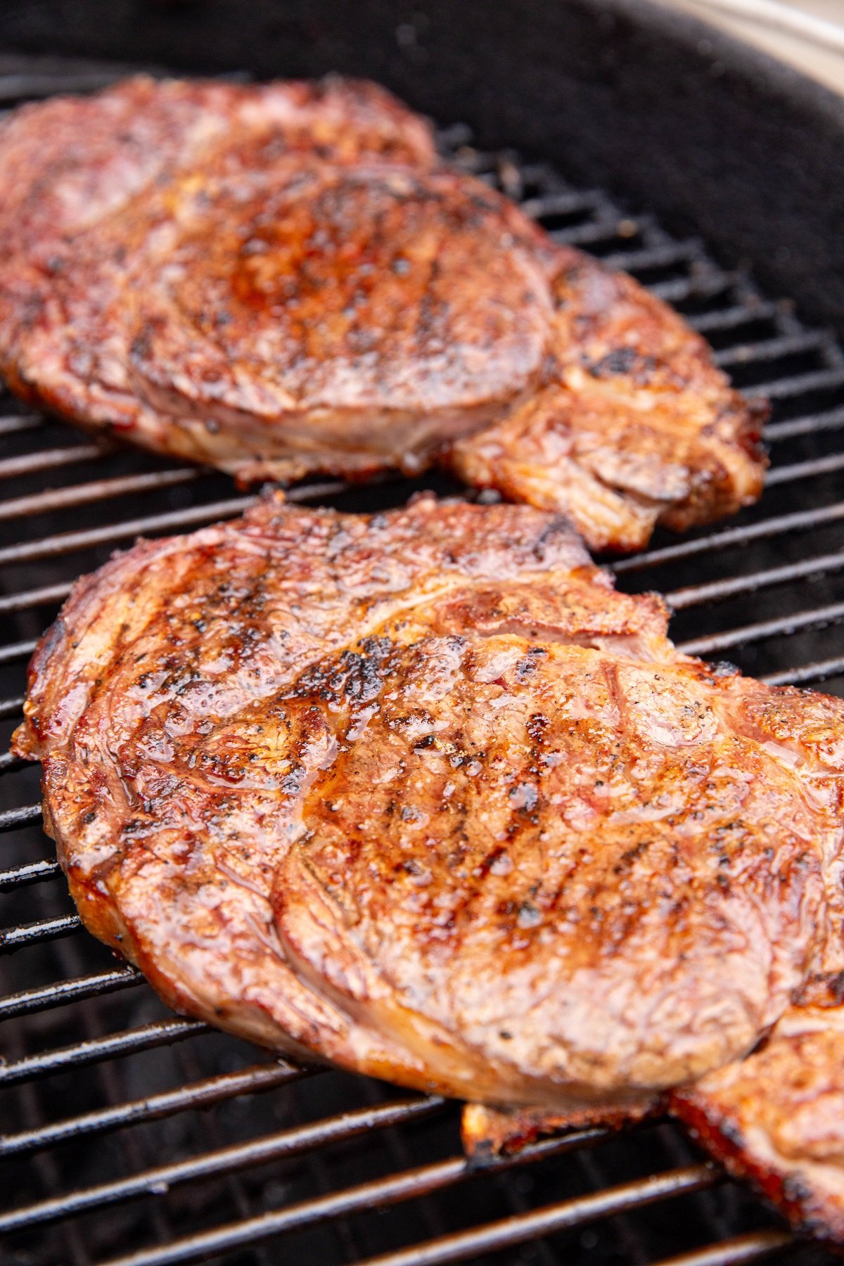 Two boneless ribeye steaks on a grill, finished and ready to eat.