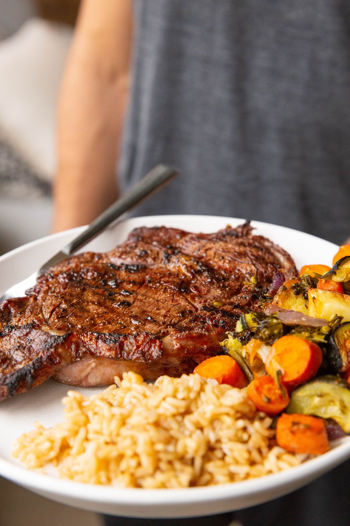 Man holding a plate of steak, rice, and vegetables.