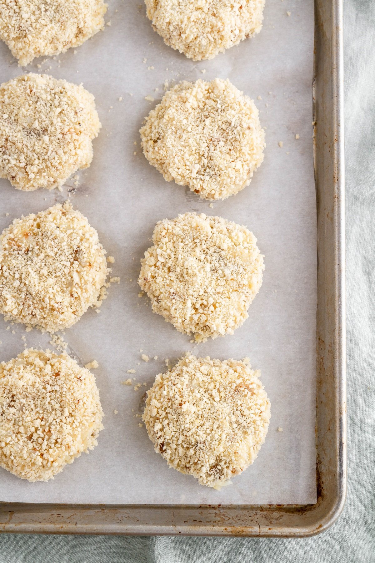 Baking sheet with potato cakes dipped in breadcrumbs, ready to be baked.