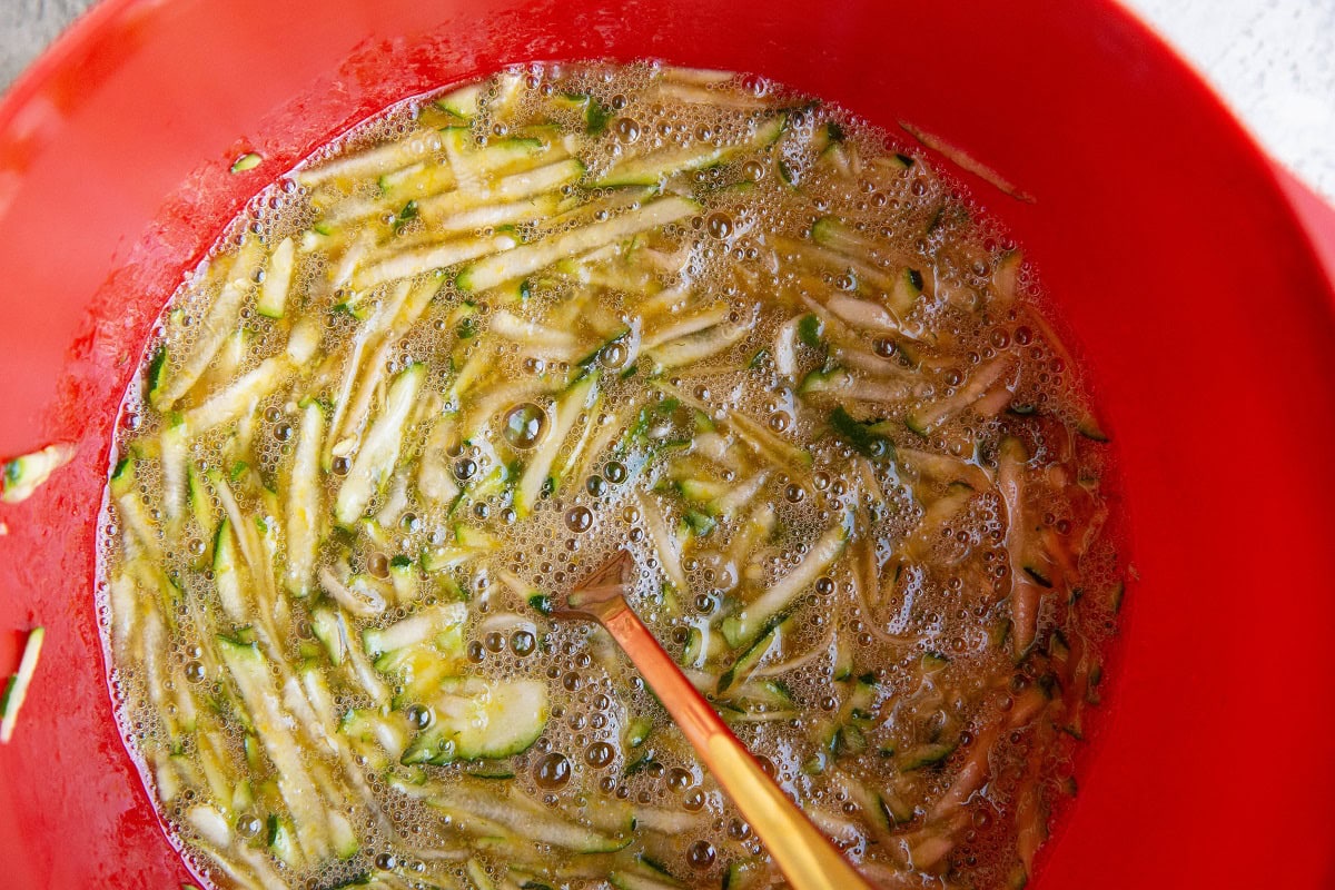 Eggs, grated zucchini, oil, and pure maple syrup in a red mixing bowl. The wet ingredients for zucchini bread.