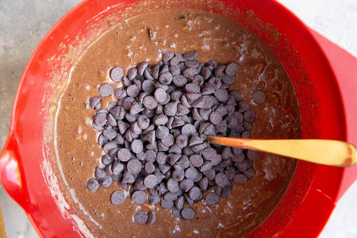 Zucchini bread batter in a red mixing bowl with chocolate chips about to be mixed in.