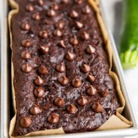 Chocolate zucchini bread in a loaf pan fresh out of the oven with a zucchini to the side.