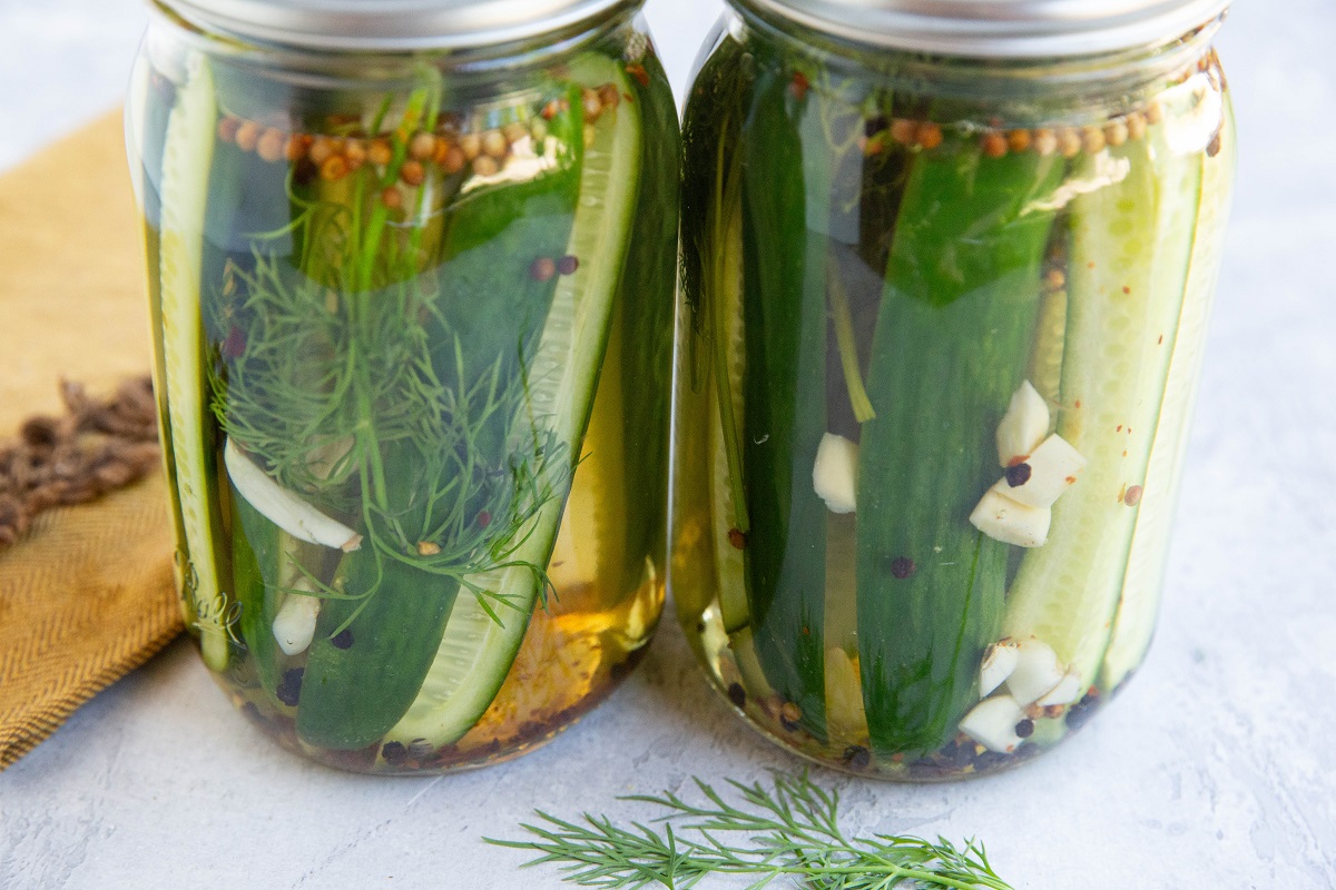 Two jars of dill pickles with a golden napkin.