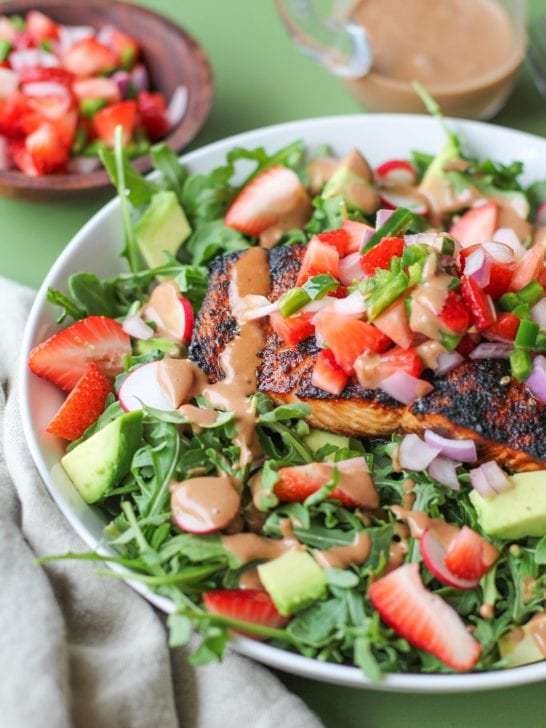 Grilled salmon in a bowl with salad ingredients, strawberry salsa and avocado on a green background.
