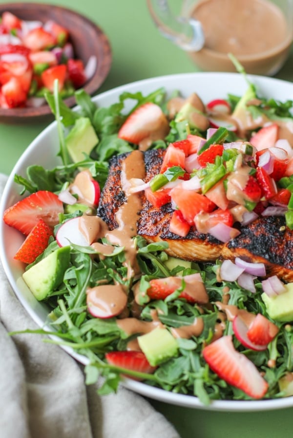 Grilled salmon in a bowl with salad ingredients, strawberry salsa and avocado on a green background.
