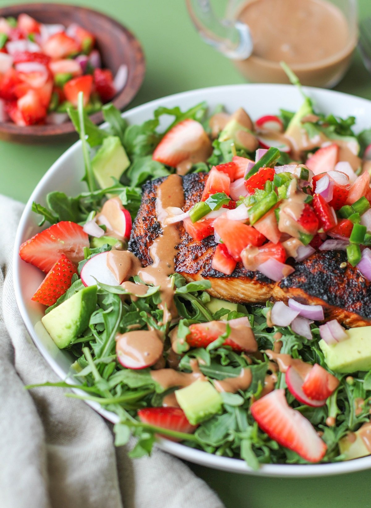 Grilled salmon in a bowl with salad ingredients, strawberry salsa and avocado on a green background.