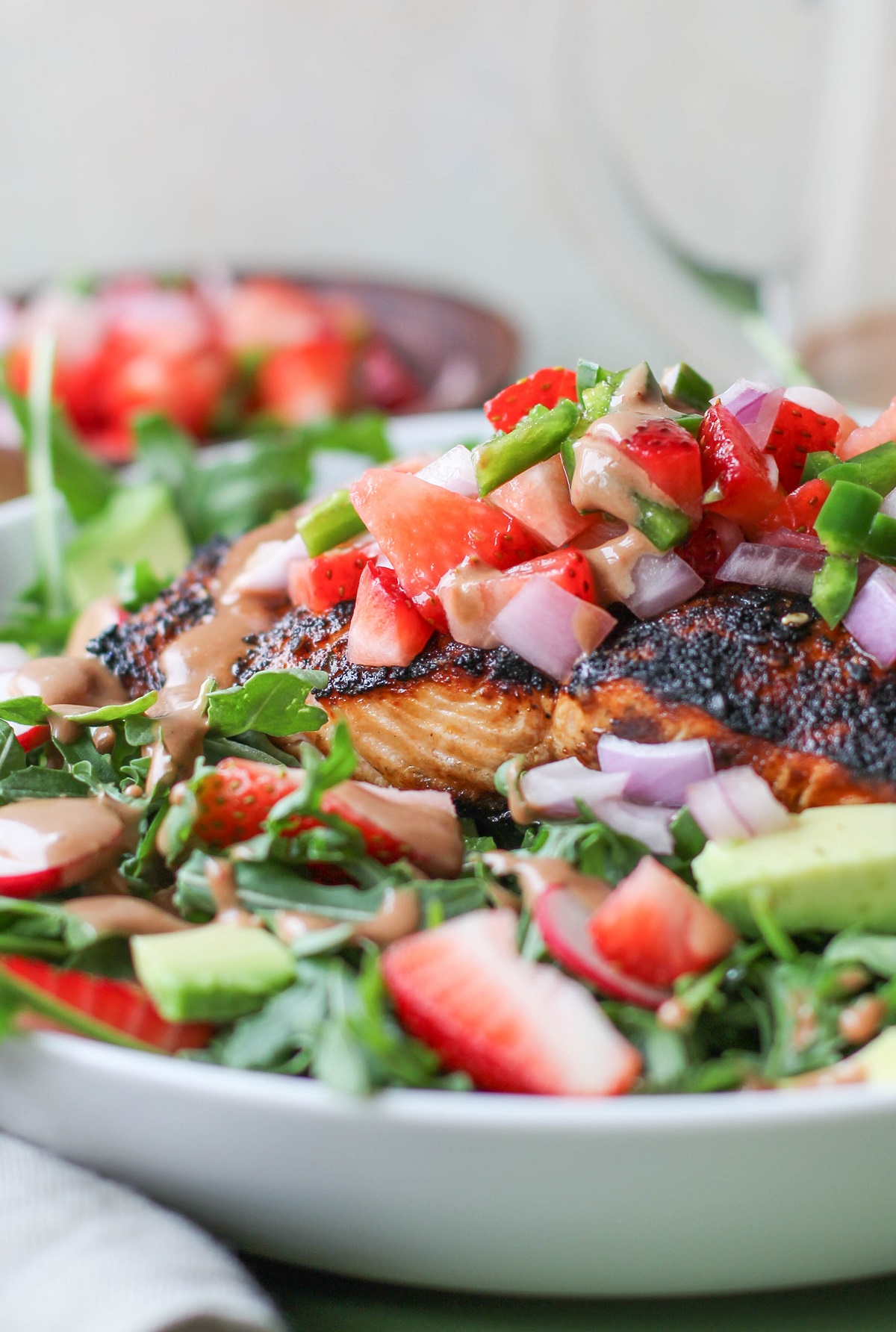 Close up on grilled salmon on a bed of salad in a white bowl with strawberry salsa on top.