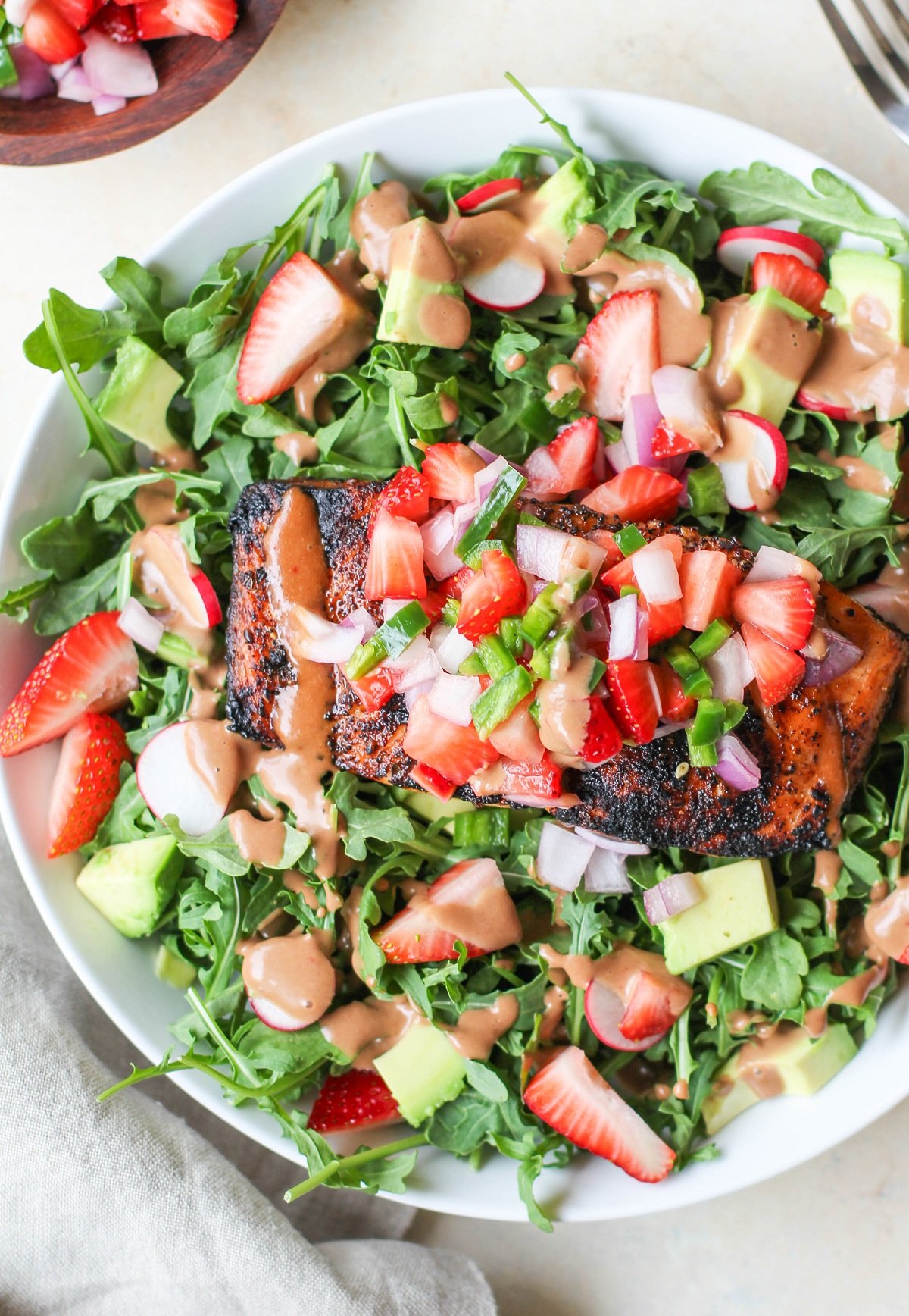 White bowl of grilled salmon and salad with dressing drizzled on top, ready to eat.