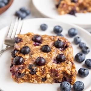 close up of a blueberry bar on a white plate with another plate of blueberry bar in the background.