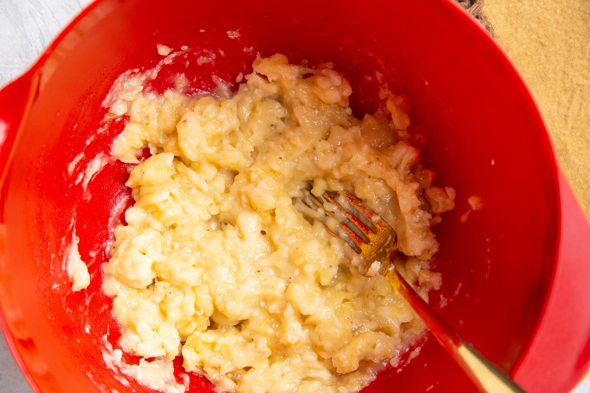 Mashed bananas in a red mixing bowl.