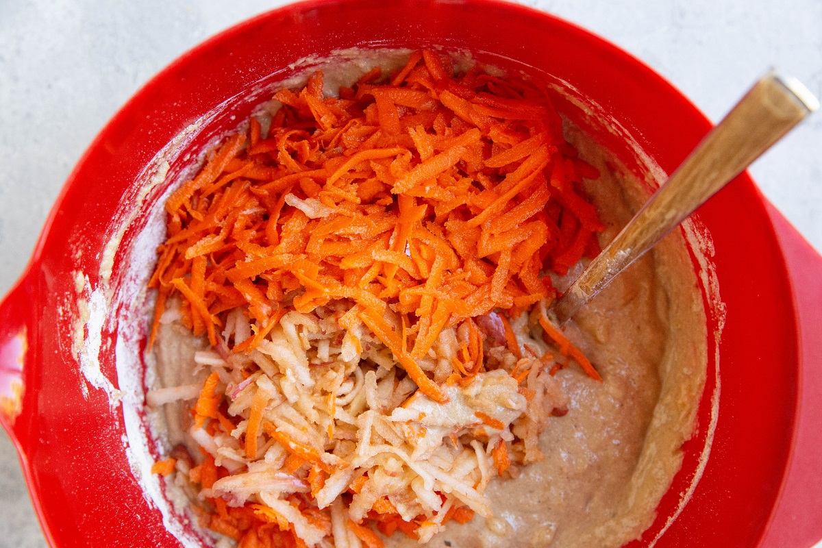 Grated carrots and apples in a mixing bowl with bread batter.