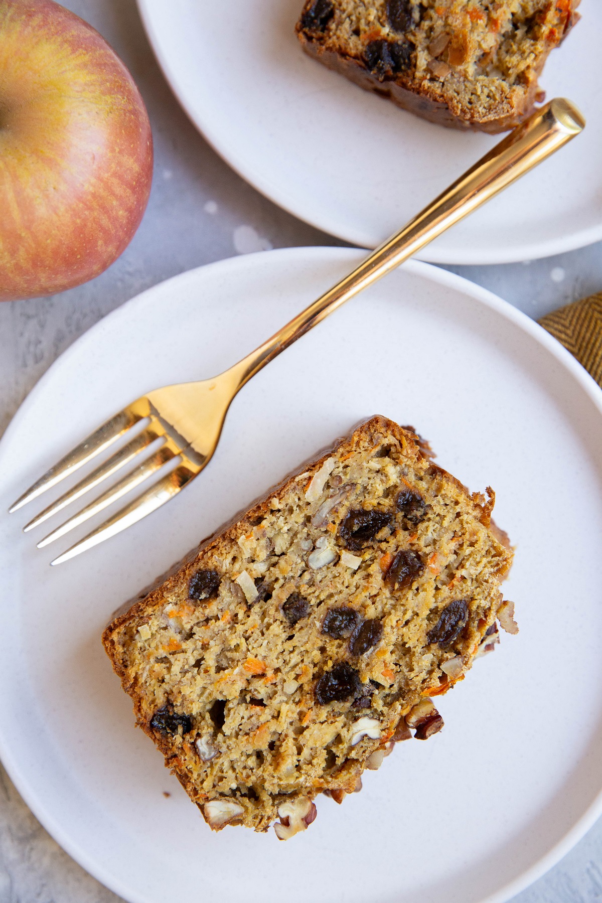 Two white plates with slices of morning glory quick bread. An apple and a fork to the side.