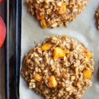 Peach oatmeal cookies on a baking sheet, fresh out of the oven with fresh peaches to the side.